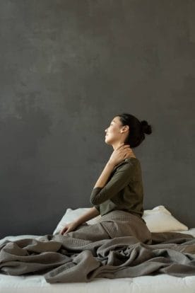 kobieta siedząca na łóżku i trzymająca się za szyję, ból pleców