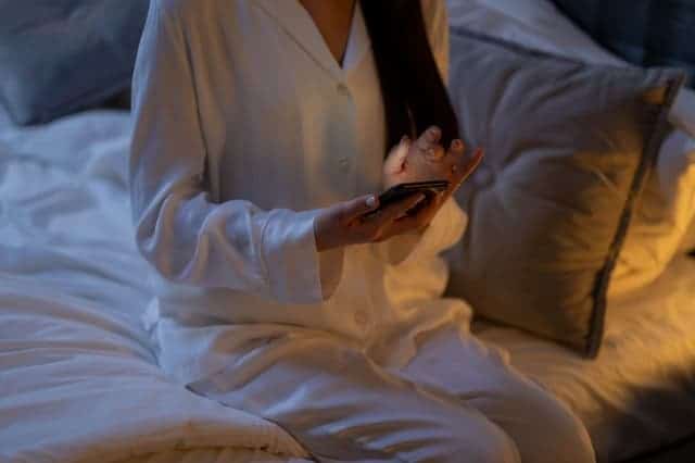mujer en pijama con smartphone en la mano sentada en la cama