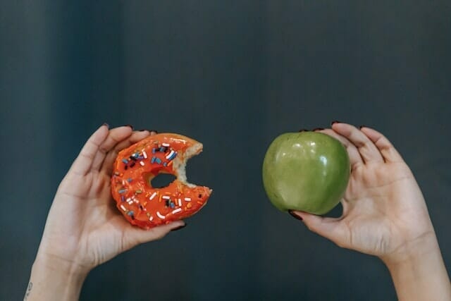  dos manos, una sosteniendo una manzana, la otra un donut